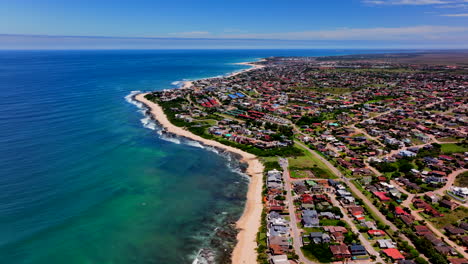 Südafrika-Jbay-Jeffreys-Bay-Luftaufnahme-Drohne-Stadt-Häuser-Atemberaubender-Weißer-Sandstrand-Epische-Brandungswelle-Gesättigtes-Wasserblau-Zerklüftete-Riffküste-Tagsüber-WSL-Corona-Open-Supers-Boneyard-Sommer-Kreisen