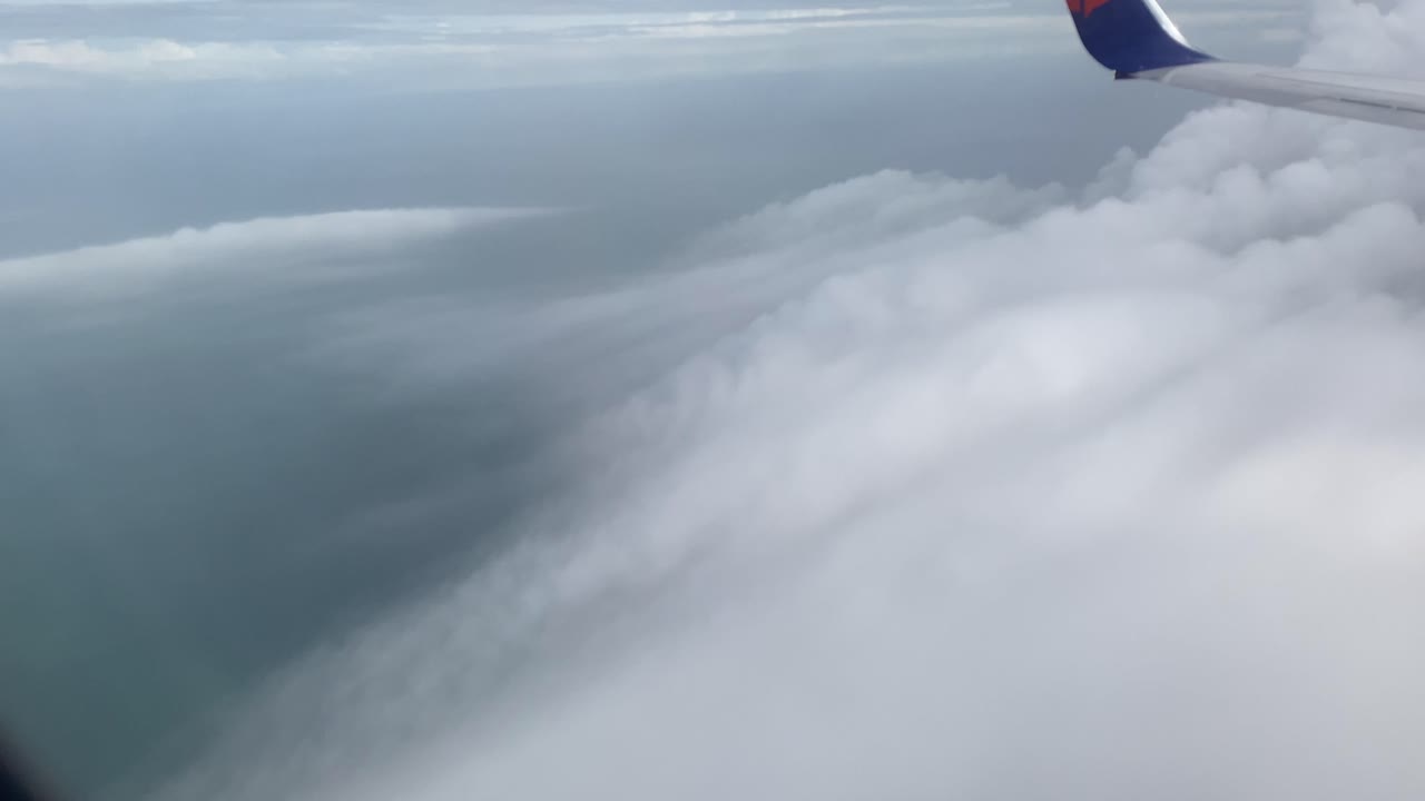 View of clouds in the sky from the window of a plane flying over the ocean.