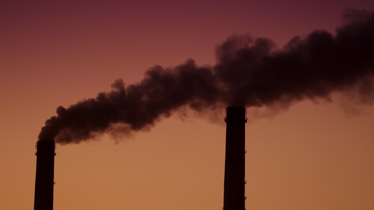 Air pollution by smoke coming out of two factory chimneys. Aerial view.