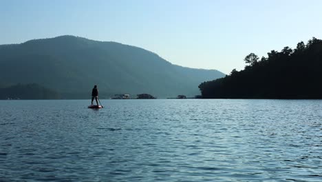 person paddleboarding on calm water with mountain backdrop