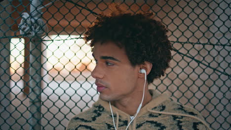 relaxed student listening headphones music in urban setting closeup. curly guy
