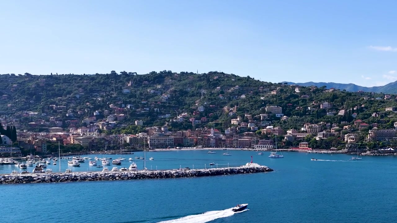 Ampia vista aerea di un motoscafo bianco che naviga su acqua blu vicino a un villaggio costiero.
