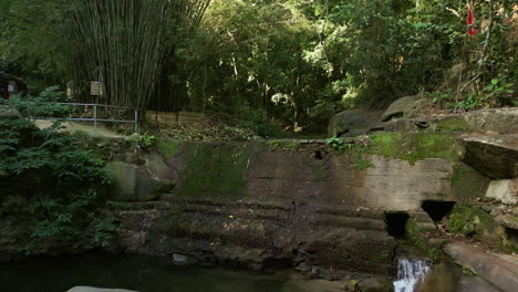 drone flies over espraiado waterfall in maricá, rio de janeiro, revealing a dense tropical forest, rocky stream, mossy stones, small dam and mysterious abandoned concrete ruins in the jungle