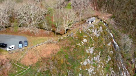 Mirador-Con-Coches-Y-Gente-En-La-Naturaleza-Con-Vistas-A-La-Cascada-En-El-Acantilado-Con-Eucaliptos-En-La-Ladera-Del-Valle