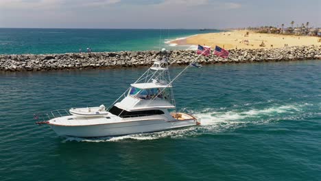 Aerial-view-of-a-large-boat,-with-American-flags-flying,-moving-through-the-channel-in-Newport-Beach,-California