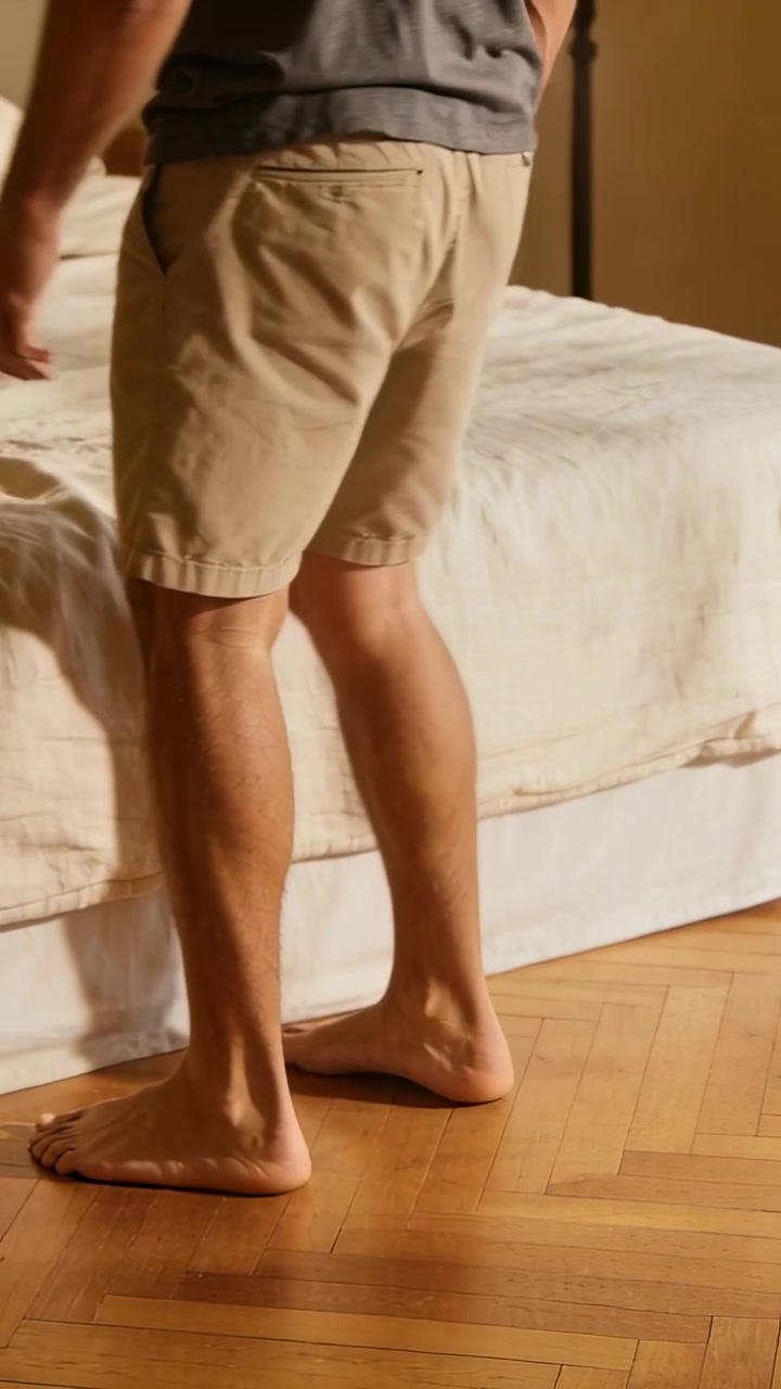 Video verticale: Uomo che cammina in pantaloni color kaki e maglietta scura in camera da letto, raggiungendo il bordo del letto e toccando il piumone.