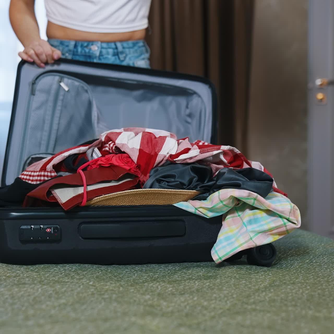 Woman closing full suitcase. Young woman packing her luggage at the end of a trip. Girl trying to close the travel bag on bed in the hotel room