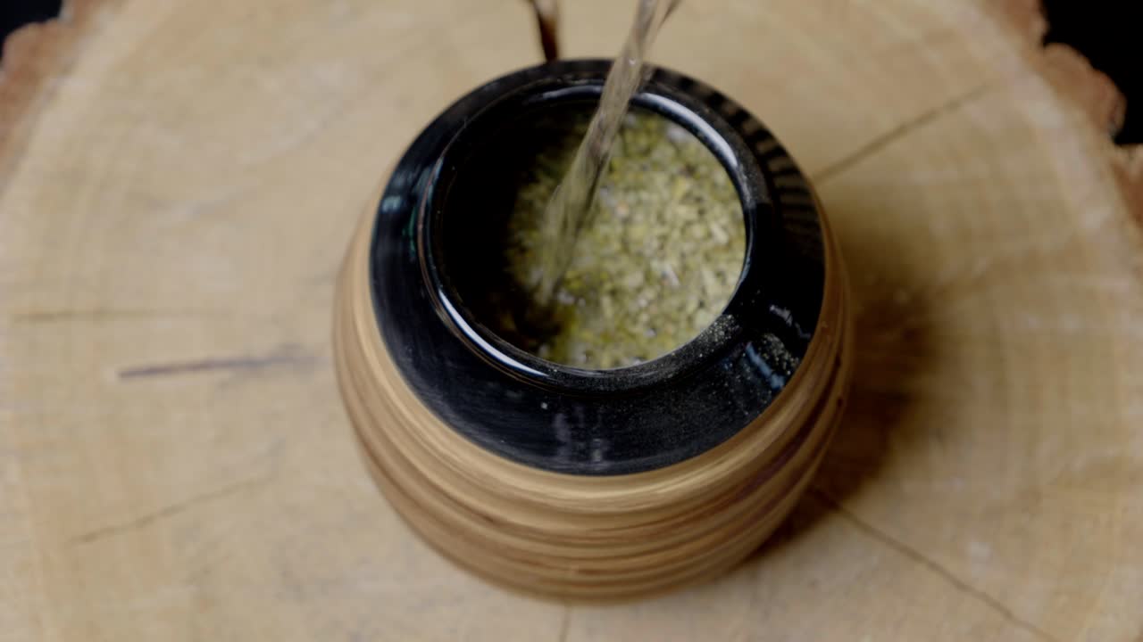 Water from a kettle is poured into the gourd with yerba mate, which is placed on a wooden circle