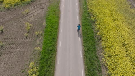 drone oblique angle follows single person biking along path at midday by yellow field