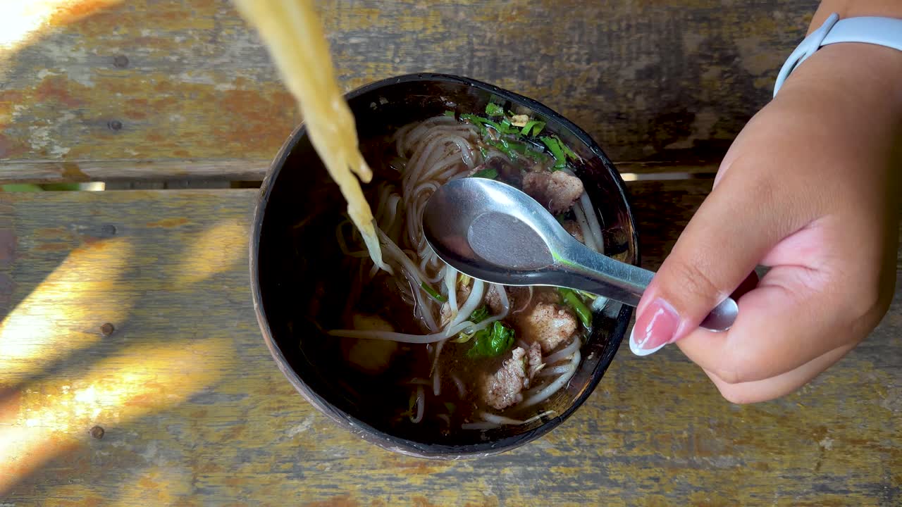 Person enjoying noodles with chopsticks and spoon