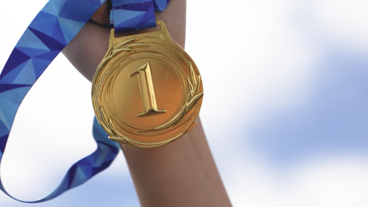Hand holding a gold medal in an outdoor setting with sky background. Symbol of success, achievement, victory, and reward. Concept of winning, motivation, and reaching personal goals