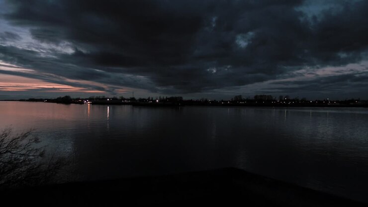 Panoramica a destra di nuvole scure su acque tranquille del fiume con nuvole e colori drammatici nel cielo al tramonto