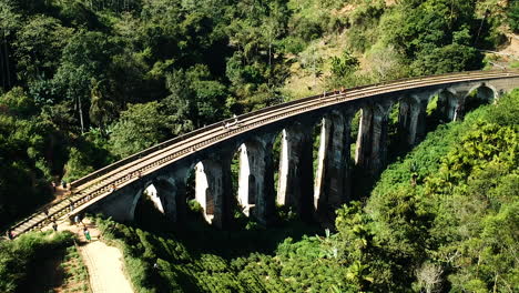 Aerial-of-famous-nine-arch-bridge-in-Ella,-Sri-Lanka-with-blue-train