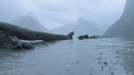 Low-angle-shot-of-the-water-rolling-into-shore-at-Milford-Sound-on-a-foggy-and-rainy-morning