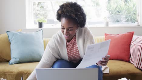 happy african american woman working at home, doing paperwork and using laptop, slow motion