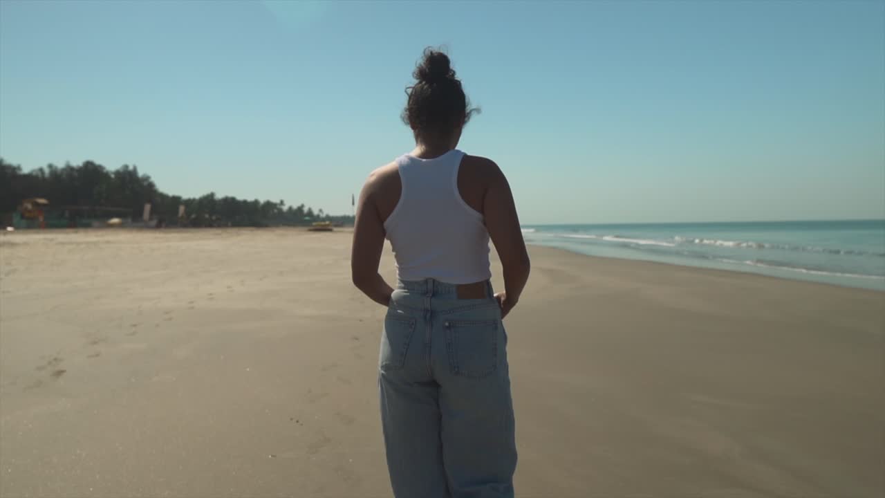 young woman strolling on the beach in jeans and a shirt, clear blue sky