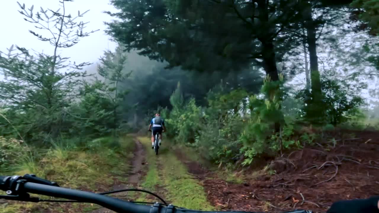 dos ciclistas andan en bicicleta por una carretera dentro de un bosque, una colina y un pueblo en guatemala, américa del norte