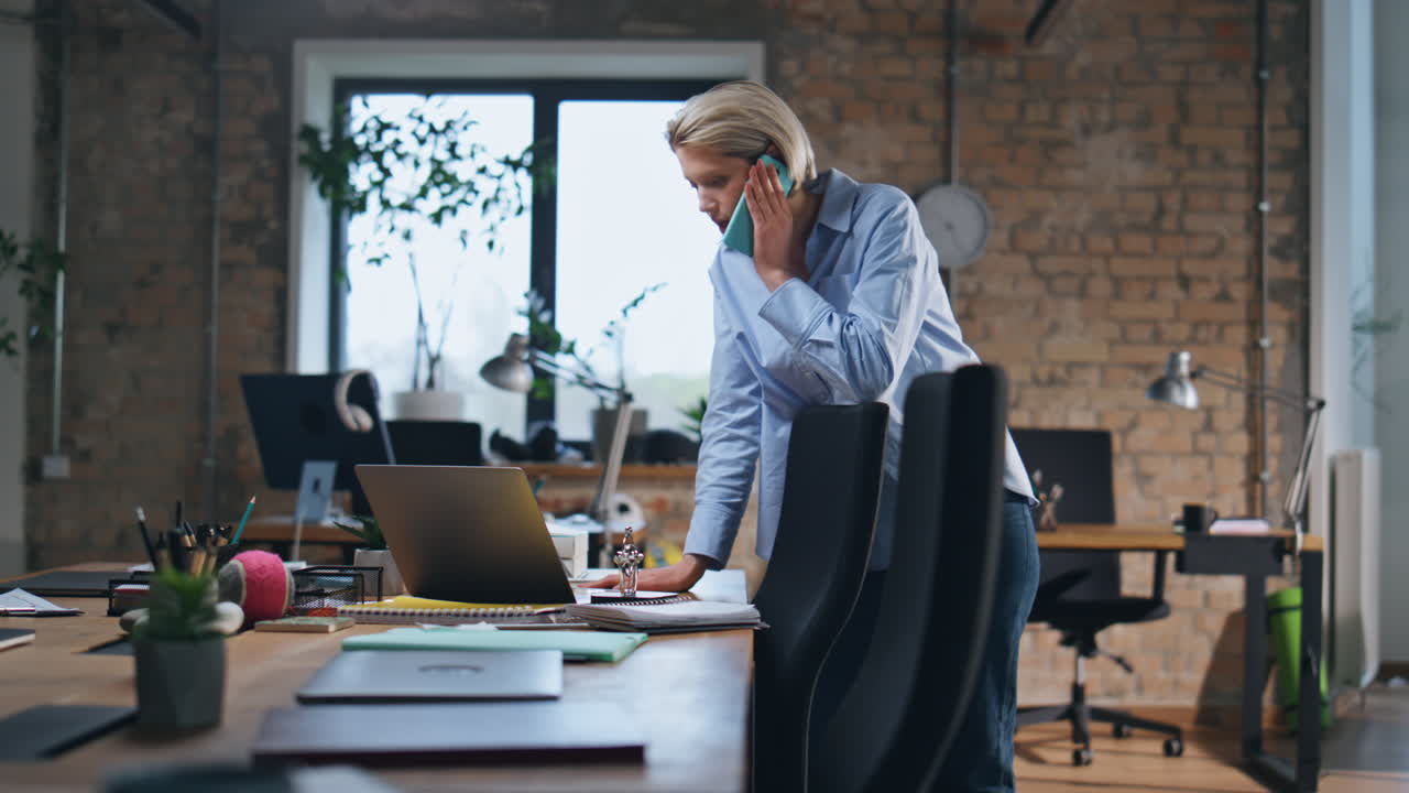 kobieta biznesu rozmawia przez telefon w pustym biurze. mądra kobieta szuka laptopa.