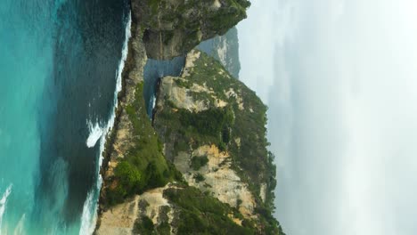 vertical slow motion panorama shot of the beautiful cliffs in front of diamond beach on nusa penida overlooking the blue sea on a beautiful morning