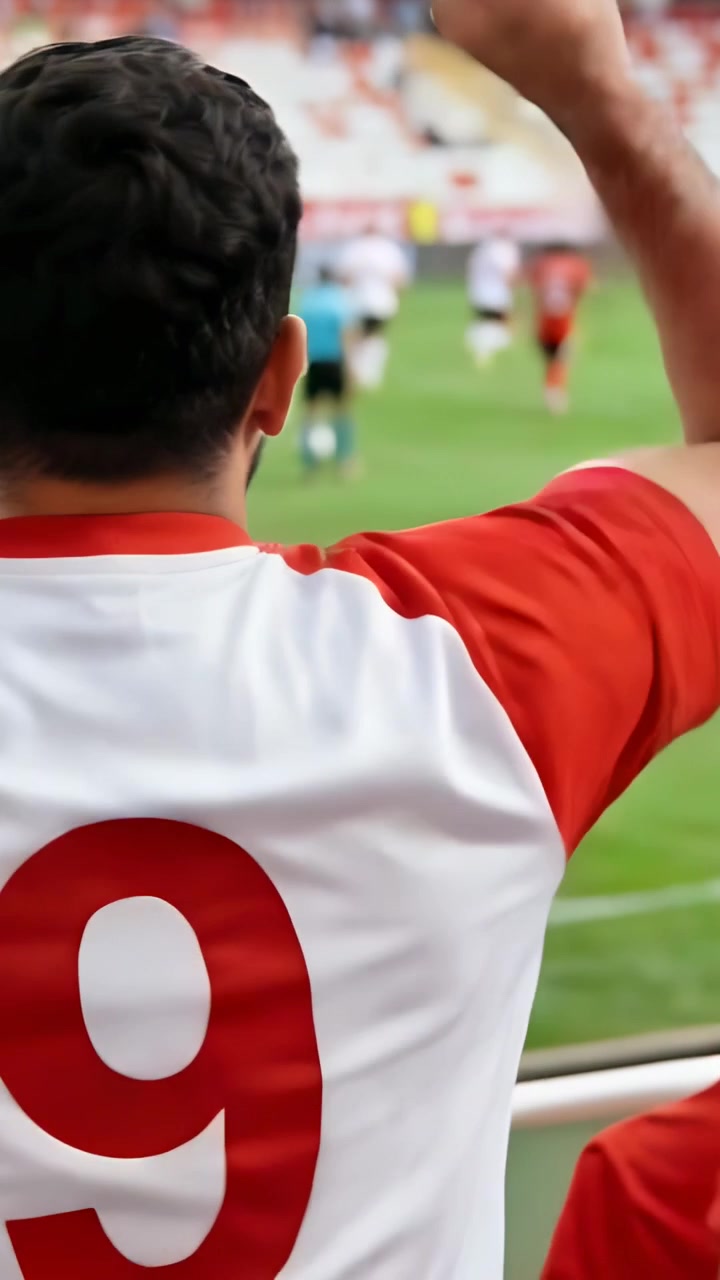 Video verticale: Tifoso esultante con maglia rosso-bianca numero 9 che alza il pugno alla ringhiera, reagendo al gioco.