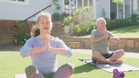 Glückliches,-Vielfältiges-älteres-Paar,-Das-Yoga-Praktiziert-Und-Auf-Matten-Im-Garten-Meditiert