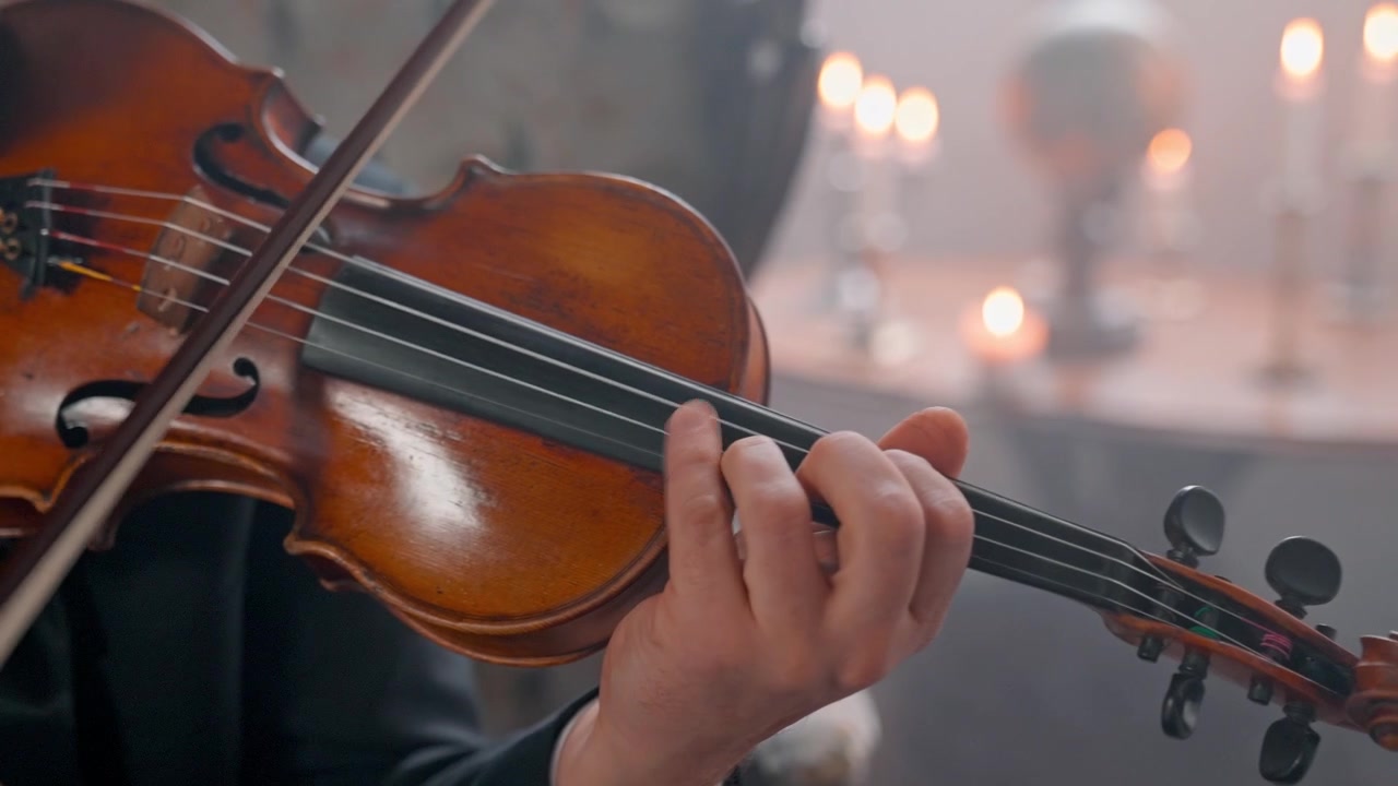 Primo piano di un musicista che suona il violino con la calda luce delle candele