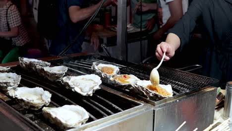 oysters being grilled and seasoned at a market