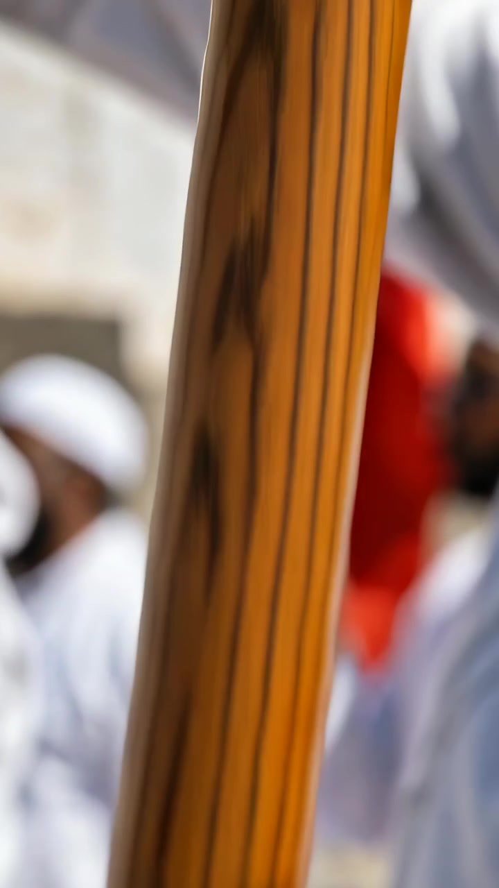 Vertical video: Gripping pole with right hand, man in white in parade while camera pulling, flags
