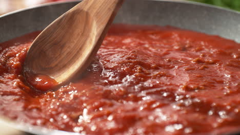 mixing tomato sauce for spaghetti bolognese or pizza with a wooden spoon in the pan - the hot dish bubbles and steams in slow motion