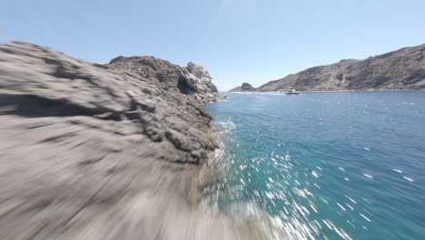 fpv drone volando bajo sobre la costa rocosa mediterránea y aguas turquesas claras