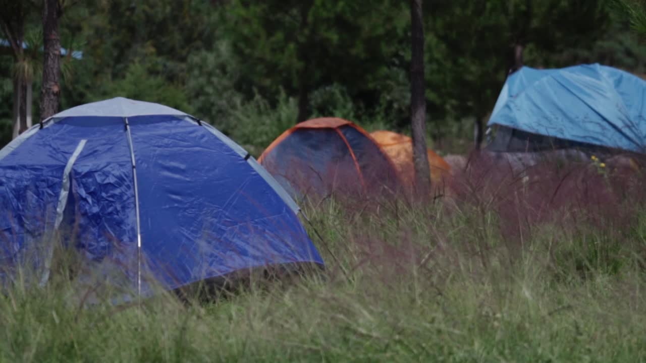 Tents set up in a field, low pan across group outdoor living space