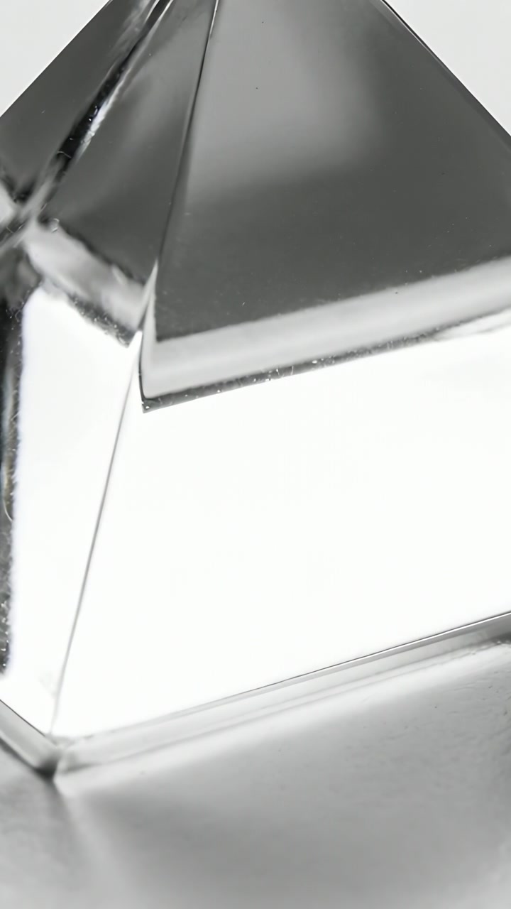 Vertical video: Showing metal pyramid reacting to subtle lighting shifts on mirror table backdrop