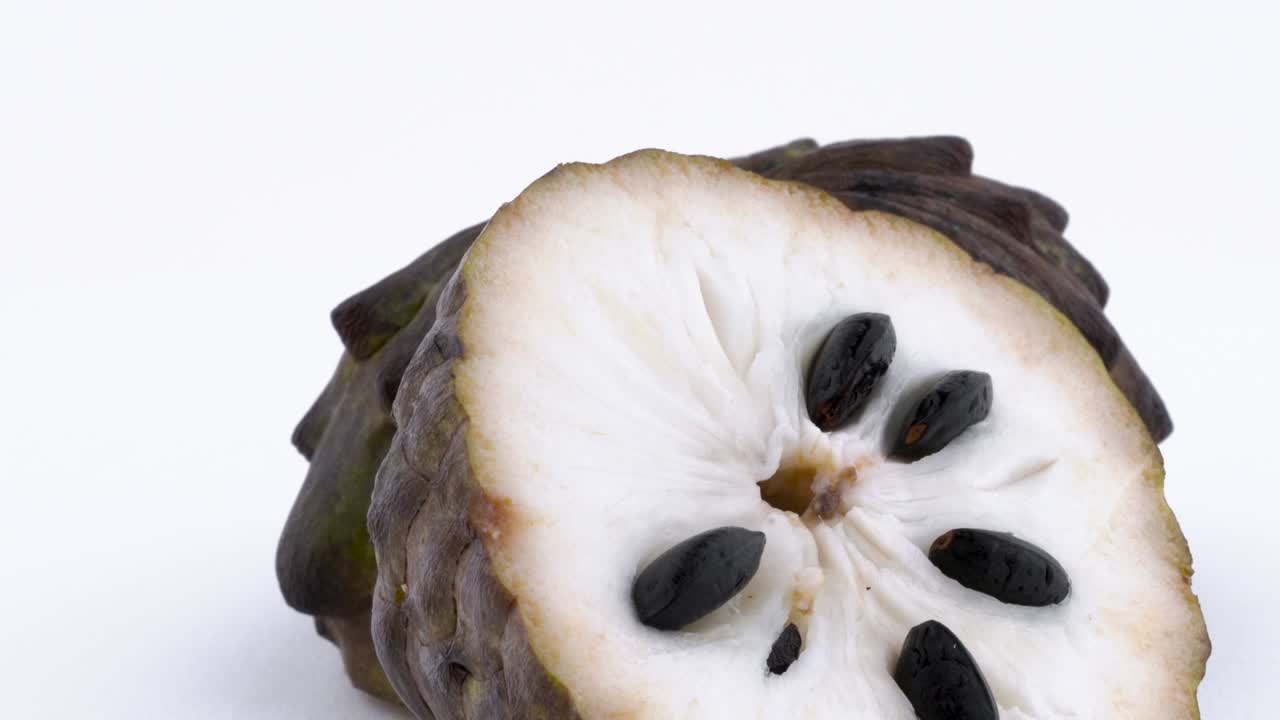 macro disparo de pulpa de fruta de manzana de azúcar con las semillas. dos mitades de fruta madura de annona. girando lentamente en la mesa giratoria aislada en el fondo blanco. primer plano.