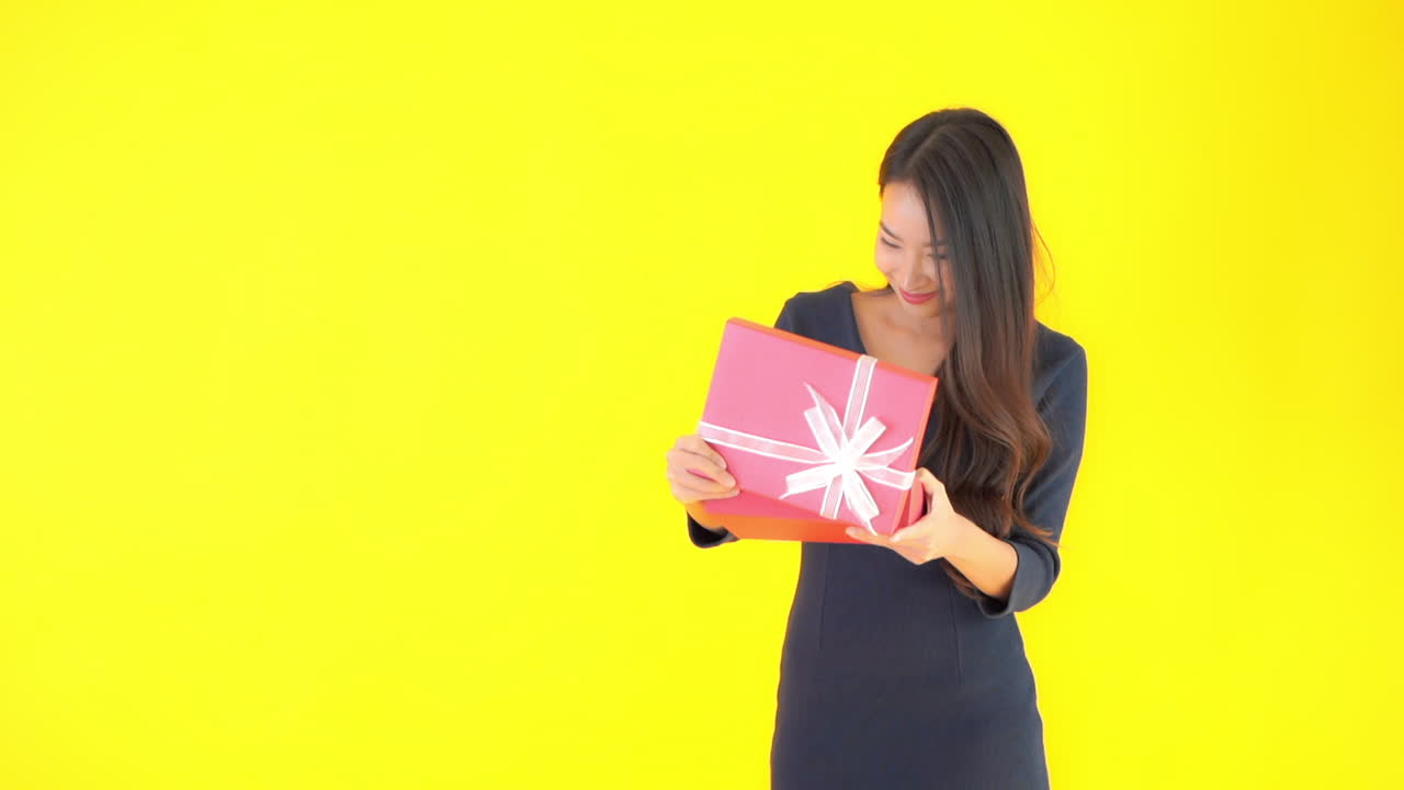 젊고 예쁜 여자가 미소로 반응하는 분홍색 종이와 흰색 레이스 활로 싸인 선물을 엽니다