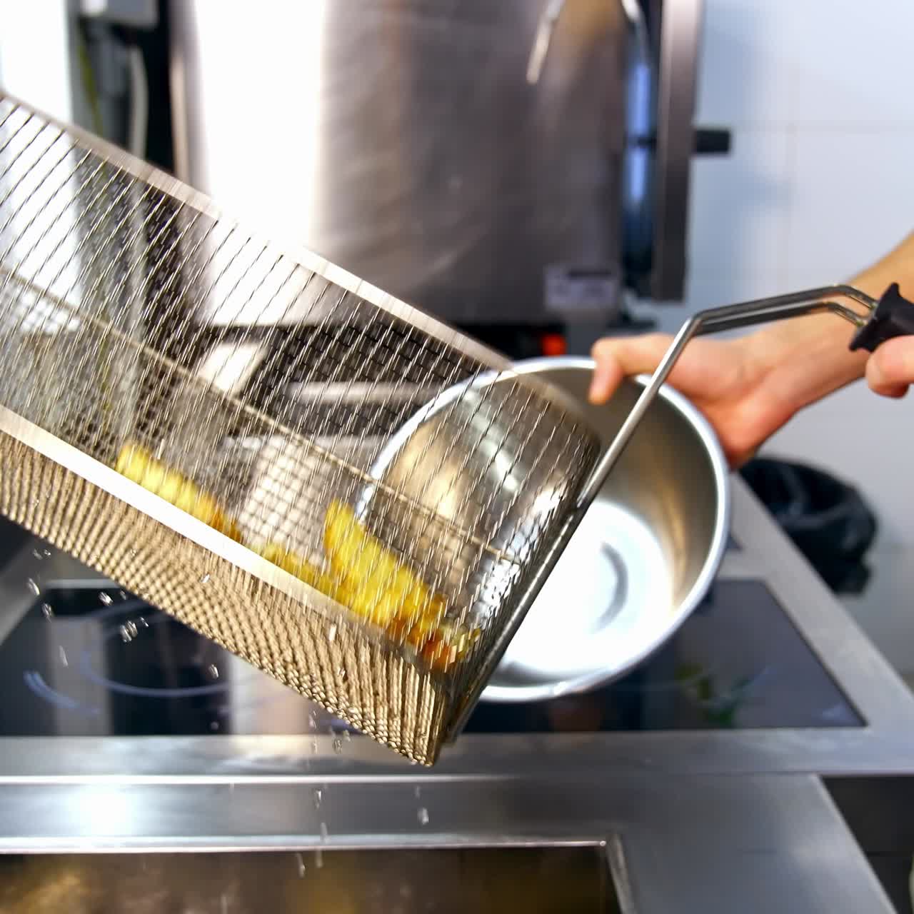 Færdige pommes frites lagt i en stor skål af rustfrit stål. Professionelt køkken i en moderne restaurant som baggrund. Kartofler stegt i olie.
