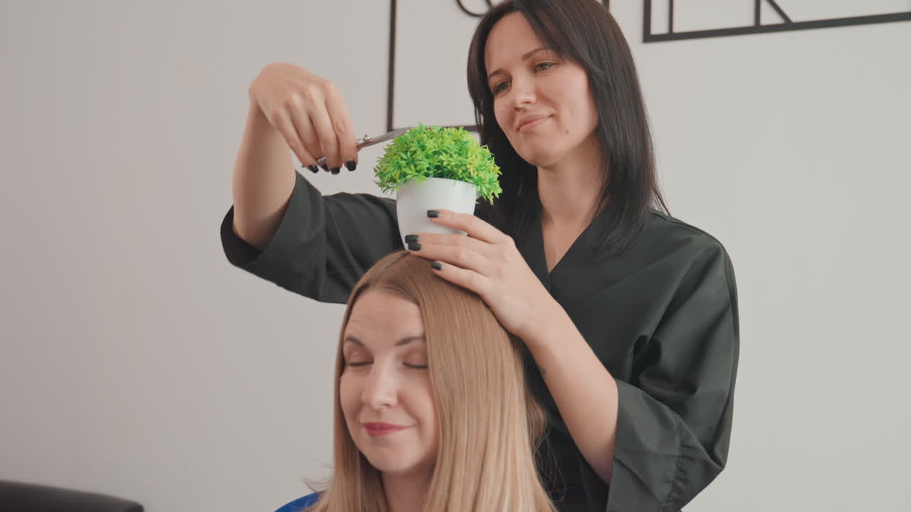 estilista corona a clienta con planta: estilista caucásica morena coloca suavemente una planta verde en maceta sobre la cabeza de una clienta caucásica rubia sentada en una silla de peluquería, estudio moderno y luminoso, ambiente de broma divertida, sonrisas