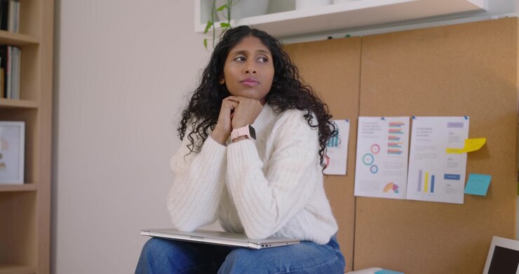 After pausing African American woman sitting at desk in wool sweater opening laptop to review chart