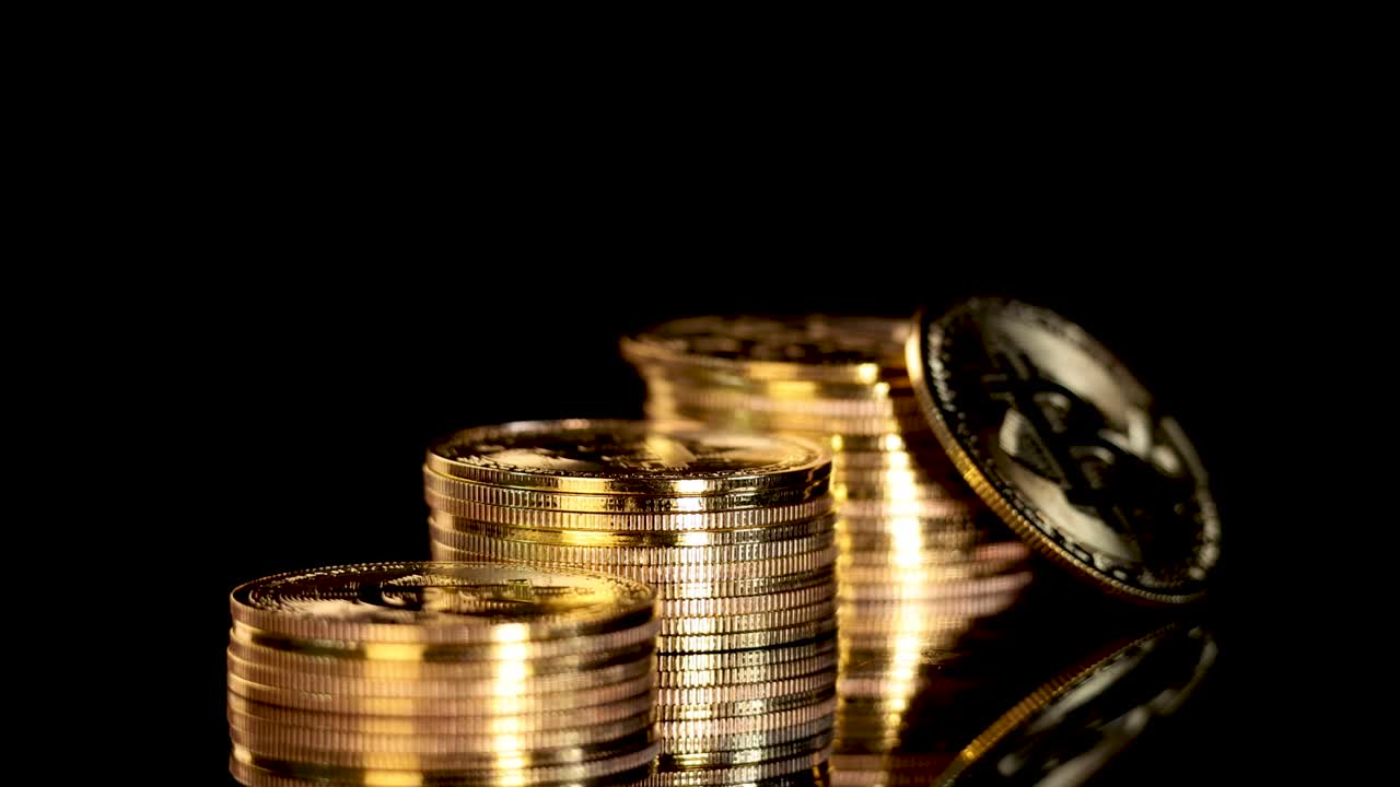 Gold coin with cryptocurrency symbol spins atop stacked coins, dramatic lighting, black background, reflective surface