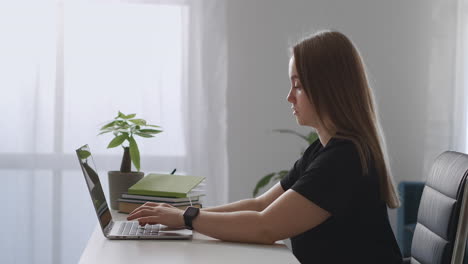 woman is typing messages in social networks using internet by laptop in home side view on young lady with notebook pressing buttons on keyboard