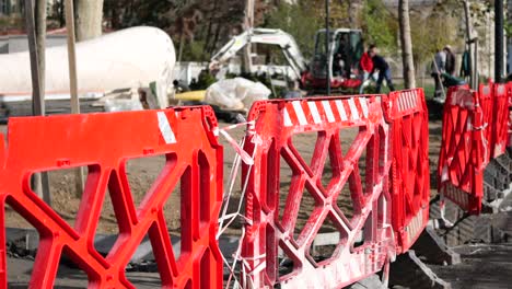 construction workers using machinery behind red plastic barriers