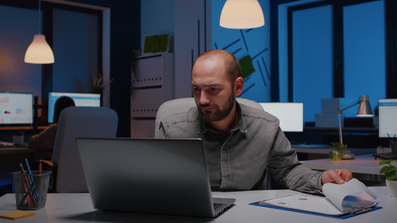 Exhausted workaholic businessman analysing marketing statistics sitting at desk table