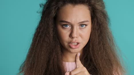 mujer caucásica de cabello rizado manteniendo el dedo sobre los labios delante de la cámara.
