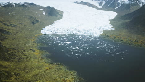 glacier calving into a serene lake surrounded by rugged mountains