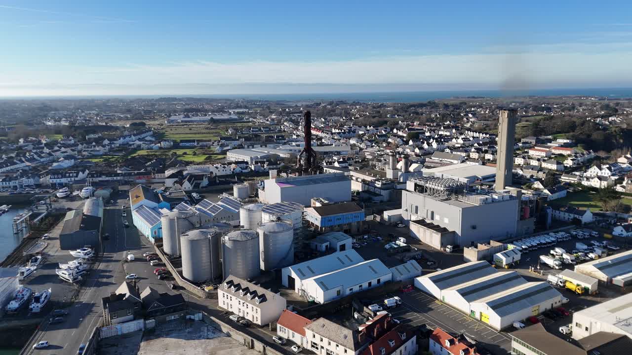 Guernsey drone flight over Industrial zone in St Sampsons pulling back from power station along Northside and harbour in bright late afternoon sunlight with blue sky and full perspective of area