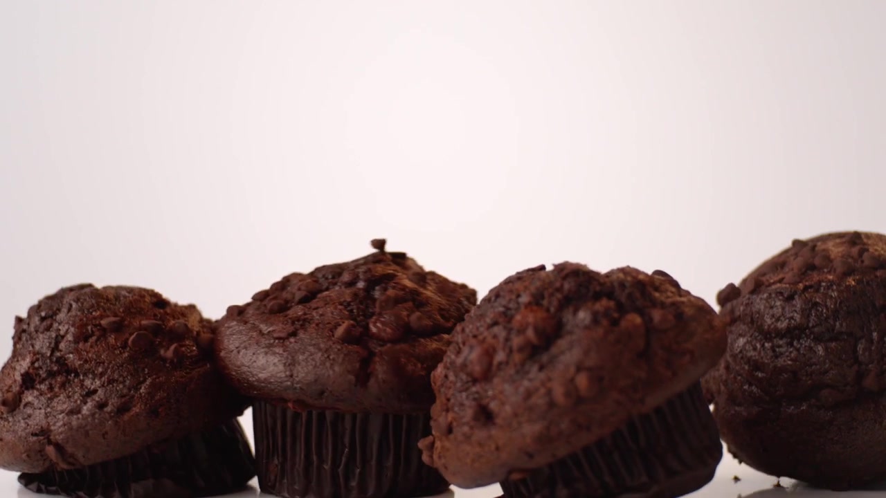 Muffin con gocce di cioccolato che rimbalzano e rotolano su uno sfondo bianco in uno scatto macro da studio al rallentatore. Contenuto per il pranzo dei bambini, pubblicità per la colazione scolastica, reel di spuntini dopo scuola