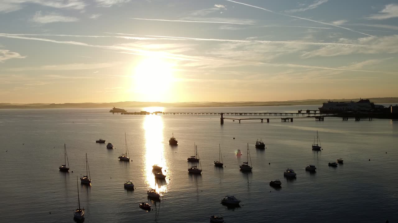 Boats silhouetted on golden shimmering harbour ocean surface aerial view descending