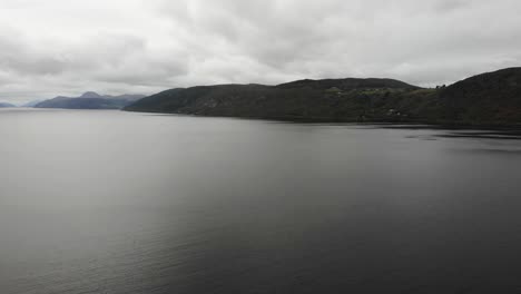 Vista-Aérea-Sobre-Las-Tranquilas-Aguas-Del-Lago-Ness-Con-Paisaje-De-Montaña-En-Segundo-Plano.