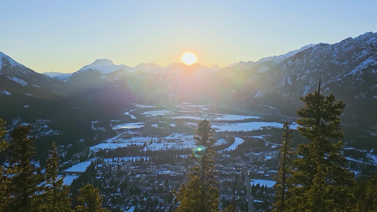 Cảnh mùa đông hùng vĩ tại Banff, Alberta, Canada, nhìn ra thị trấn và Thung lũng Bow với những ngọn núi phủ đầy tuyết, cây thông, mặt trời rực rỡ, phong cảnh dãy núi Rockies ấn tượng và những khung cảnh du lịch tuyệt đẹp.