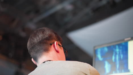close-up of young man wearing glasses focusing on monitor, modern studio environment with blue and white lights visible in background. creative professional working in tv production setting
