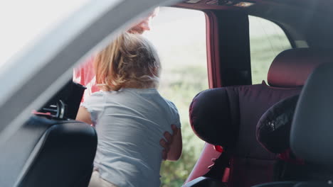 father carrying young daughter and putting her into child seat in rear of car for journey